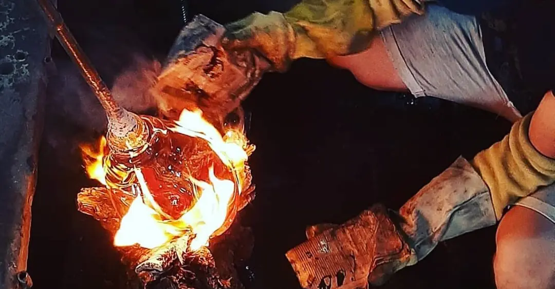 Manos enguantadas trabajando vidrio incandescente sobre el fuego.